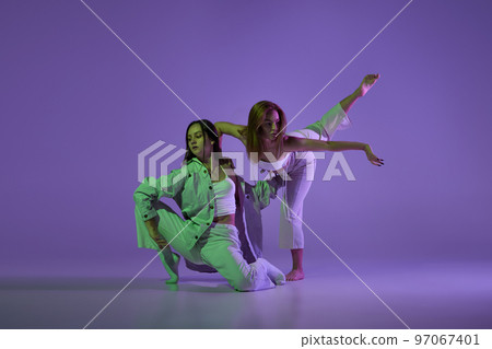 Studio footage of dancing young girls. Stylish performance. Two young women in expressive contemporary dance isolated over purple background. Studio footage of dancing young girls. Stylish performance. Two young women in expressive contemporary dance isolated over purple background. 97067401