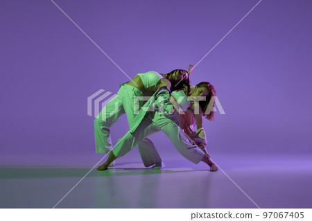 Dance performance. Stylish female dancers at contemporary choreography dance class isolated over crystal purple background. Style, youth, music and fashion 97067405