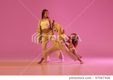 Modern dance art. Young girls, couple of dancers in sports style clothes dancing experimental dances isolated over light pink background in neon. Concept of music, emotions, dance 97067406