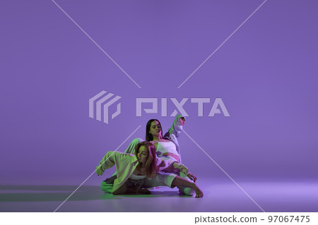 Dance performance. Stylish female dancers at contemporary choreography dance class isolated over crystal purple background. Style, youth, music and fashion 97067475