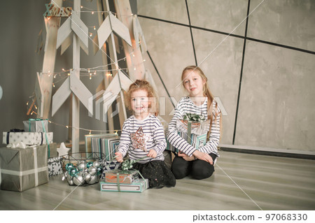 little sisters are looking at Christmas presents sitting in the modern living room little sisters are looking at Christmas presents sitting in the modern living room 97068330