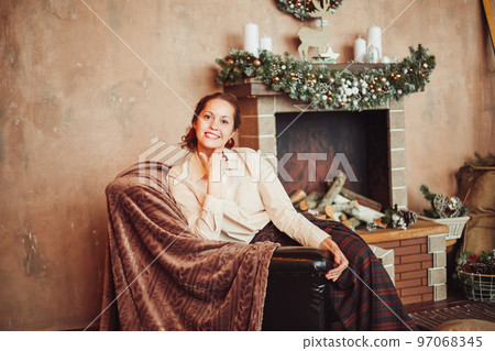 young woman sitting by the fireplace in a cozy living room 97068345
