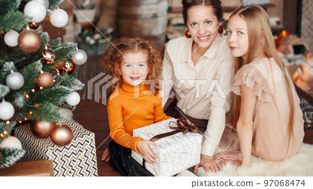 mother and her daughters opening a gift box near the Christmas t 97068474