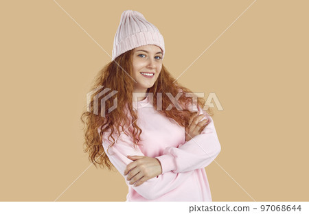 Smiling redhead girl with curly long hair wearing in pink sweatshirt and hat on beige background. Smiling redhead girl with curly long hair wearing in pink sweatshirt and hat on beige background. 97068644