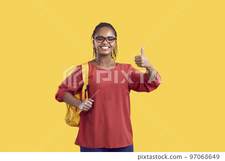 Happy african american female student in glasses showing thumb up isolated on yellow background. Happy african american female student in glasses showing thumb up isolated on yellow background. 97068649