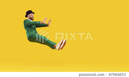 Happy man in a green suit and a black hat floating in the air on a yellow copy space background Happy man in a green suit and a black hat floating in the air on a yellow copy space background 97068655