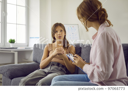 Teenage girl sitting on sofa and answering questions that therapist or psychologist asks 97068773