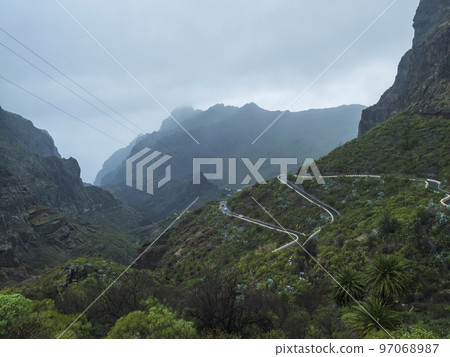Dramatic lush green landscape with winding curvy mountain road towards Masca village situated in a picturesque valley, Tenerife, Canary Islands, Spain. rainy day, moody sky Dramatic lush green landscape with winding curvy mountain road towards Masca village situated in a picturesque valley, Tenerife, Canary Islands, Spain. rainy day, moody sky 97068987