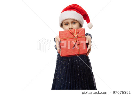 Selective focus on a stylish red gift box in the hands of a cute baby girl, holding out a Christmas present on camera, isolated on white background. Boxing Day. Xmas and New Year's celebration concept 97076591
