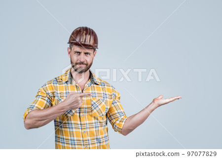 handsome man foreman in helmet and checkered shirt presenting product, copy space, advertisement. handsome man foreman in helmet and checkered shirt presenting product, copy space, advertisement. 97077829