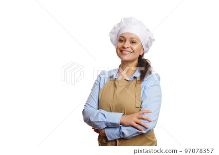 Cheerful female baker confectioner, pastry chef, female cook, waitress in chef's hat and apron, smiling a cheerful toothy smile looking at camera, isolated on white background. Copy advertising space Cheerful female baker confectioner, pastry chef, female cook, waitress in chef's hat and apron, smiling a cheerful toothy smile looking at camera, isolated on white background. Copy advertising space 97078357