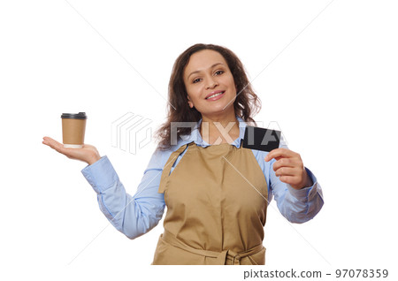 Isolated portrait on white background of a pretty woman in casual blue shirt and beige chef apron, holding a takeaway drink in paper cup and showing on camera a credit card with copy advertising space Isolated portrait on white background of a pretty woman in casual blue shirt and beige chef apron, holding a takeaway drink in paper cup and showing on camera a credit card with copy advertising space 97078359