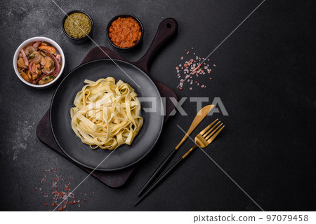 Delicious fresh pasta with pesto sauce and seafood on a black plate Delicious fresh pasta with pesto sauce and seafood on a black plate 97079458