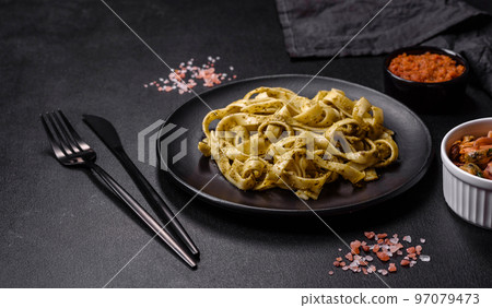 Delicious fresh pasta with pesto sauce and seafood on a black plate 97079473