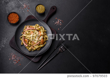 Delicious fresh pasta with pesto sauce and seafood on a black plate 97079503