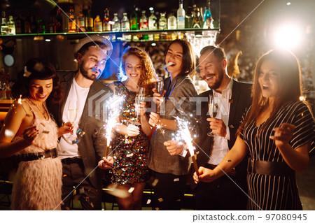 Glowing sparkles in hands. Group of happy people enjoying party with fireworks. Winter holiday. 97080945