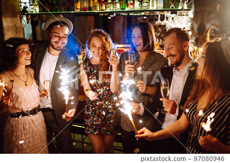 Glowing sparkles in hands. Group of happy people enjoying party with fireworks. Winter holiday. 97080946
