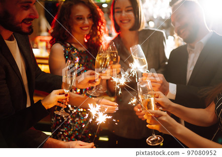 Glowing sparkles in hands. Group of happy people enjoying party with fireworks. Winter holiday. 97080952