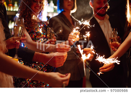 Glowing sparkles in hands. Group of happy people enjoying party with fireworks. Winter holiday. Glowing sparkles in hands. Group of happy people enjoying party with fireworks. Winter holiday. 97080986