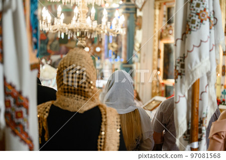 Two women are standing in the church, their heads are covered with scarves. 97081568