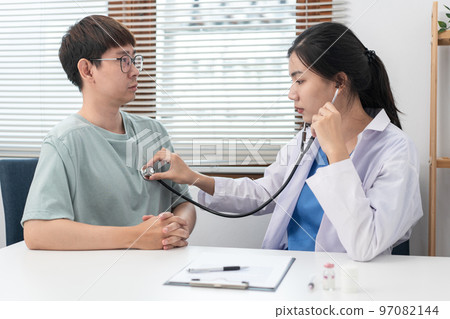 Female doctor physician is examines heart and lungs of male patient with a stethoscope to check Female doctor physician is examines heart and lungs of male patient with a stethoscope to check 97082144
