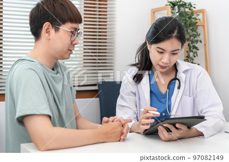 Female doctor physician is taking notes on tablet and writing prescription while asking symptom Female doctor physician is taking notes on tablet and writing prescription while asking symptom 97082149