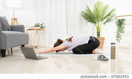 Young woman is taking yoga online class on laptop and practicing yoga with balasana or child pose 97082443