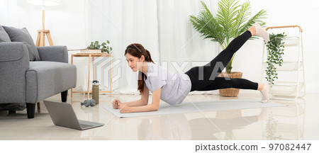Young woman is watching yoga lesson online on laptop to practicing yoga with plank pose and stretching Young woman is watching yoga lesson online on laptop to practicing yoga with plank pose and stretching 97082447