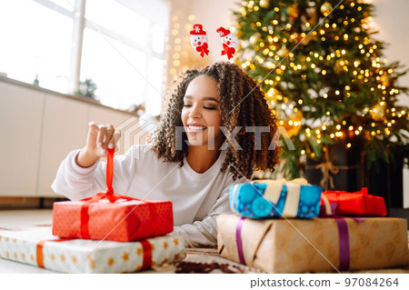 Portrait of young woman in santa claus hat with gift at the Christmas tree. Christmas. New year's. 97084264