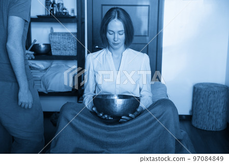 Woman holding Tibetan singing bowl in sound therapy in spa center 97084849