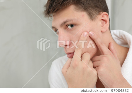 Teen guy with acne problem squeezing pimple in bathroom, closeup 97084882