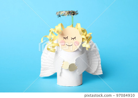 Toy angel made of toilet paper hub on light blue background Toy angel made of toilet paper hub on light blue background 97084910