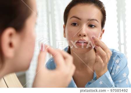 Teen girl applying acne healing patch near mirror in bathroom 97085492