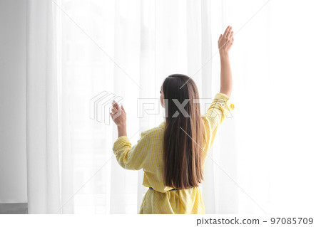 Young woman near window with curtains indoors Young woman near window with curtains indoors 97085709