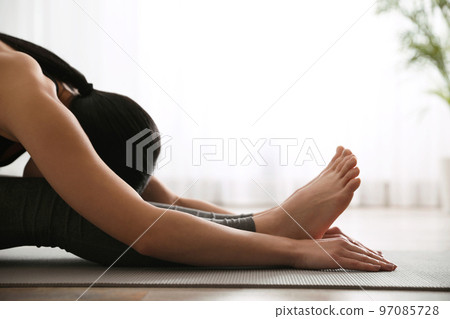 Young woman practicing seated forward bend asana in yoga studio, closeup. Paschimottanasana pose 97085728