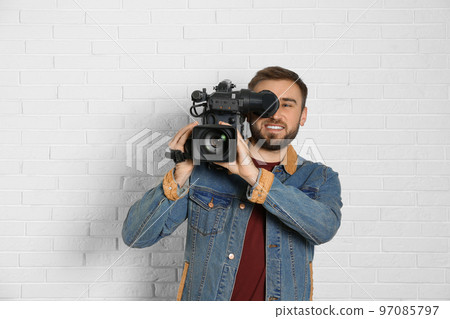 Operator with professional video camera near white brick wall 97085797