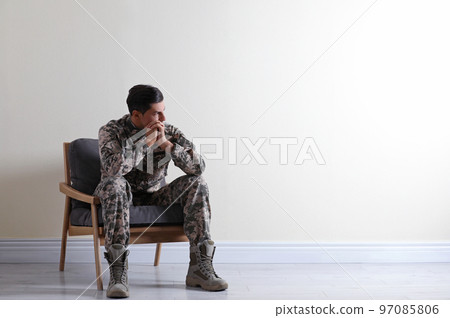 Stressed military officer sitting in armchair near white wall indoors. Space for text Stressed military officer sitting in armchair near white wall indoors. Space for text 97085806