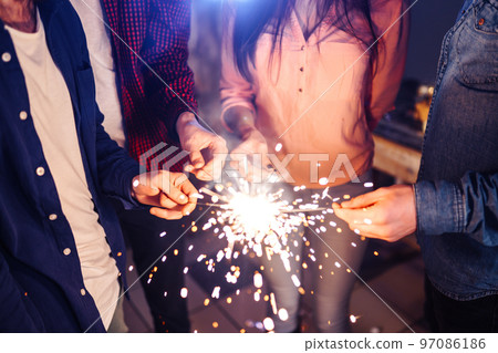 Group of friends having fun with sparklers. young people laugh. celebrating New Year together. 97086186