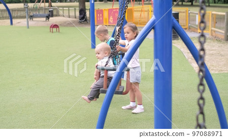 Funny Little Preschool Chubby Girl Older Sister Rides Younger Newborn Infant Brother Boy On Swing. Baby Playing On Playground. Kids Entertainment, Childhood, Child Development, Happy Family Concept 97088971