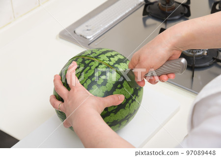 [A middle-aged housewife cuts a watermelon; there is a gas stove] 97089448