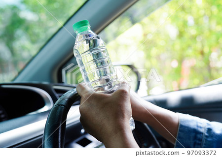 Asian woman driver hold cold water for drink in car, dangerous and risk an accident. 97093372