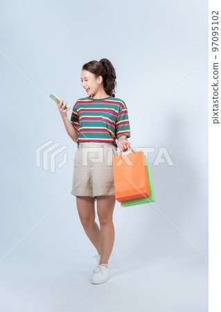 Upbeat attractive smiling asian woman walking in mall, shopping, holding bags and smartphone, calling cab, standing gray background 97095102