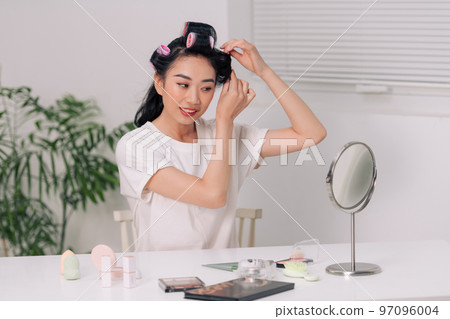 Happy woman applying hair rollers on beautiful healthy hair. Happy woman applying hair rollers on beautiful healthy hair. 97096004