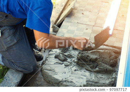 Worker builder lays tiles around building. Professional bricklayer with trowel at work on summer 97097717