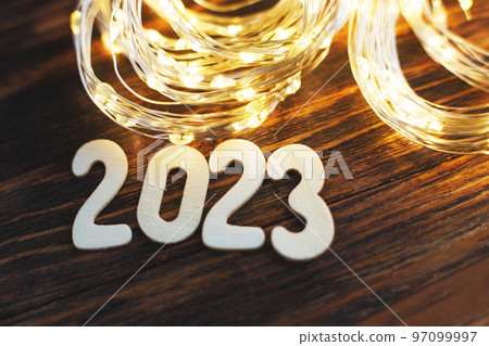wooden number 2023 on christmas shiny wooden background. with sparkle festive gold garland 97099997