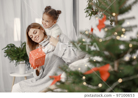 People reparing for Christmas. Mother playing with her daughter. Family is resting in a festive room. Child in a sweater sweater. 97100653