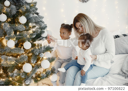 People reparing for Christmas. Mother playing with her daughters. Family is resting in a festive room. Child in a sweater sweater. People reparing for Christmas. Mother playing with her daughters. Family is resting in a festive room. Child in a sweater sweater. 97100822