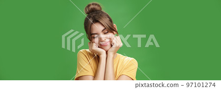 Tender sensual timid european girl in yellow t-shirt leaning head on shoulder touching cheeks with hands closing eyes and smiling with soft grin feeling nostalgic and romantic over green background Tender sensual timid european girl in yellow t-shirt leaning head on shoulder touching cheeks with hands closing eyes and smiling with soft grin feeling nostalgic and romantic over green background 97101274