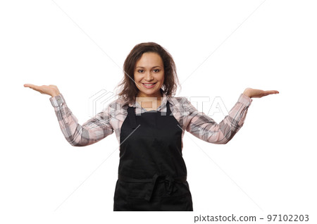 Charming multi-ethnic woman waitress barmaid, in professional uniform holds a copy space on her hands palms up, cutely smiles a cheerful toothy smile looking at camera, isolated over white background 97102203