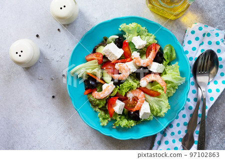 The concept of healthy and dietary food. Greek salad with shrimps and vegetables on a light stone or slate table. Top view flat lay background. Copy space. 97102863